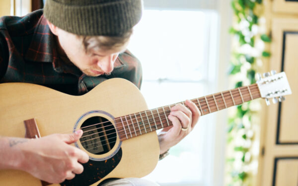 Persona tocando una guitarra acústica Martin mientras interpreta una melodía con técnica fingerstyle en un ambiente iluminado.